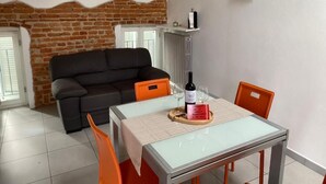 Un comedor con una mesa de vidrio, sillas color naranja, un sofá negro y una pared de ladrillo.