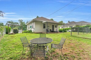 A residential property with a covered patio, a dining table with chairs, and a house in the background.