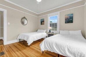 A bedroom with two single beds, a large window, and a mirror on the wall.