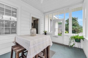 A covered porch with a table and chairs, a potted plant, and a view of the outdoors.