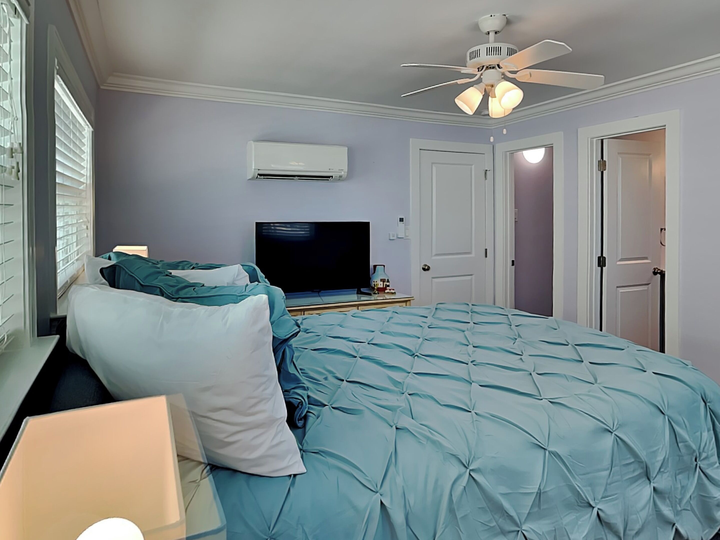 Ein Schlafzimmer mit Bett, Deckenventilator, Klimaanlage, Fernseher und einer Tür.