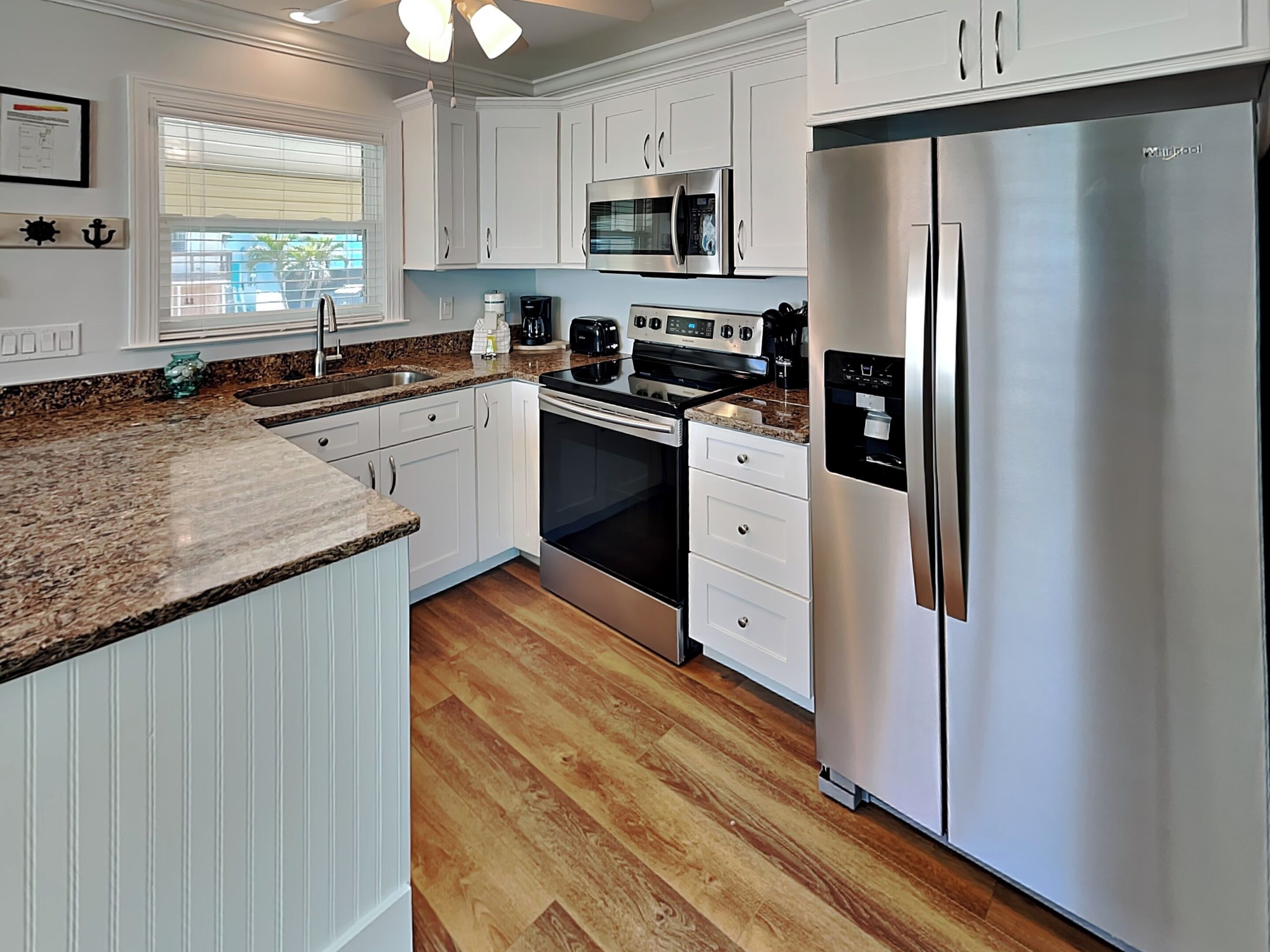 A kitchen with white cabinets, stainless steel appliances, a granite countertop, and a window with blinds.