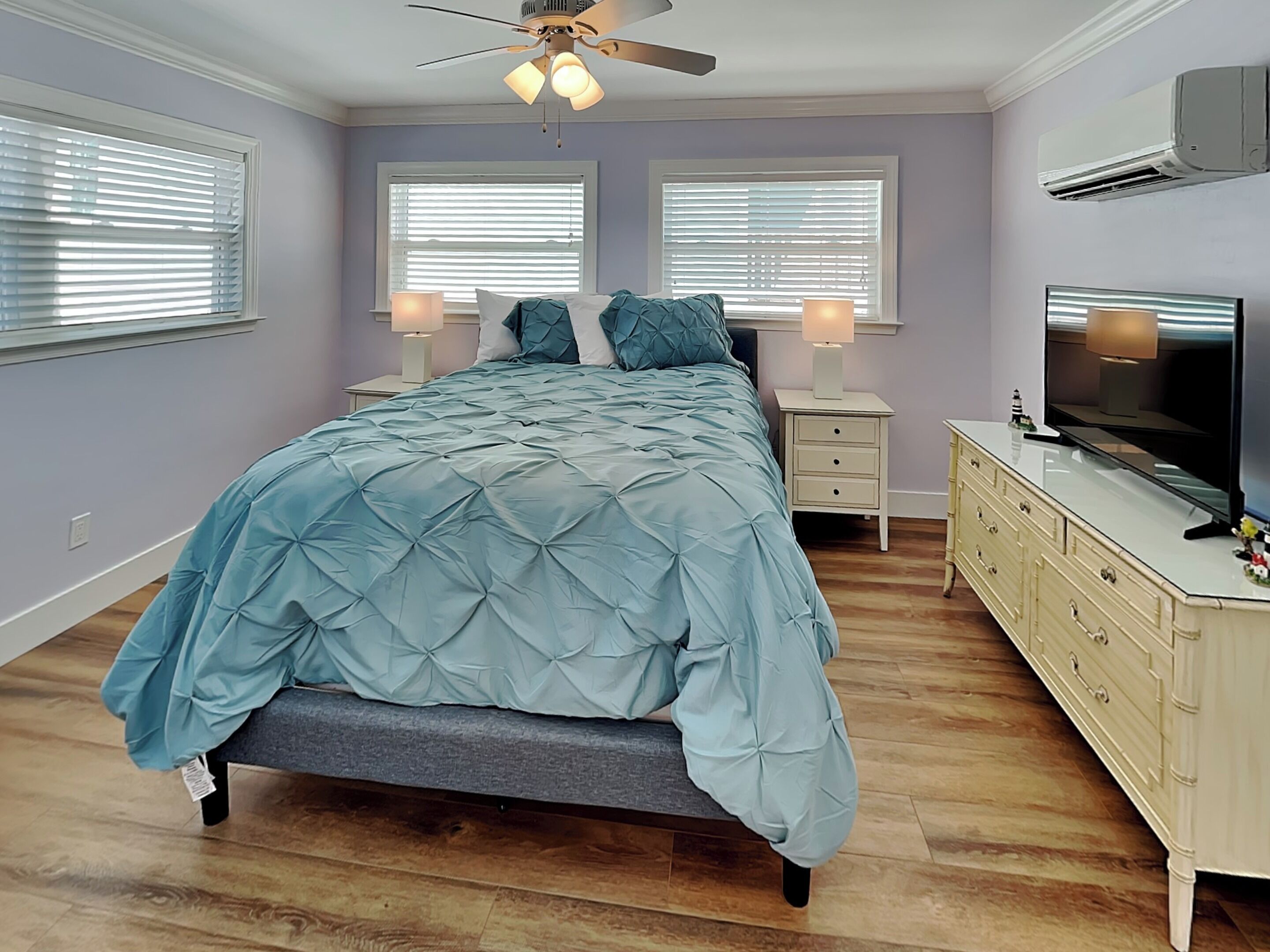 Une chambre à coucher comprenant un lit, des tables de chevet, une commode, un téléviseur et un ventilateur de plafond.