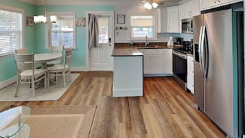 A kitchen with white cabinets, a stainless steel refrigerator, and a dining area with a table and chairs.