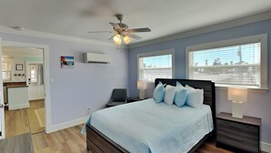 Une chambre à coucher comprenant un lit, un ventilateur de plafond, deux tables de chevet avec des lampes et une fenêtre avec des stores.