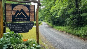 A rustic wooden sign with a logo and text for Mulberry Gap, indicating amenities like home cooked meals, hot showers, and a hot tub.