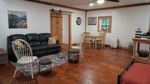 A living room with a black leather sofa, a dining table with chairs, a ceiling fan, and a wooden door.