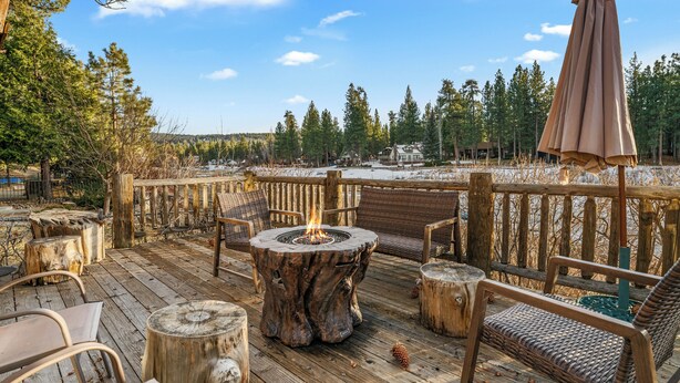 A wooden deck with a fire pit, wicker furniture, and a view of a snowy landscape. - Blue Lagoon Lakefront (Big Bear Lake)