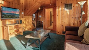 A wooden cabin interior with a television, a sofa, a table, and a staircase leading to an upper level. - Blue Lagoon Lakefront (Big Bear Lake)