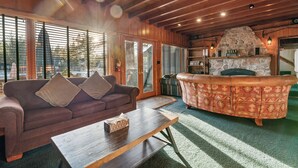 A cozy living room with a wooden ceiling, a stone fireplace, a sofa, and a coffee table. - Blue Lagoon Lakefront (Big Bear Lake)