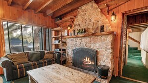 A cozy room with a stone fireplace, wooden furniture, and a staircase leading to another level. - Blue Lagoon Lakefront (Big Bear Lake)
