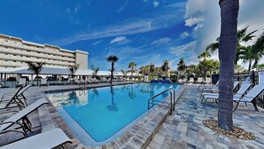 A swimming pool with lounge chairs and palm trees, surrounded by a hotel building. - Riviera Club 204 by Distinctive Beach Rentals (Fort Myers Beach)