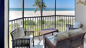 A balcony with a view of a beach and palm trees. - Riviera Club 204 by Distinctive Beach Rentals (Fort Myers Beach)