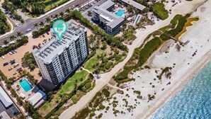 An aerial view of a beachfront hotel with a swimming pool, beach access, and a parking area. - Riviera Club 204 by Distinctive Beach Rentals (Fort Myers Beach)
