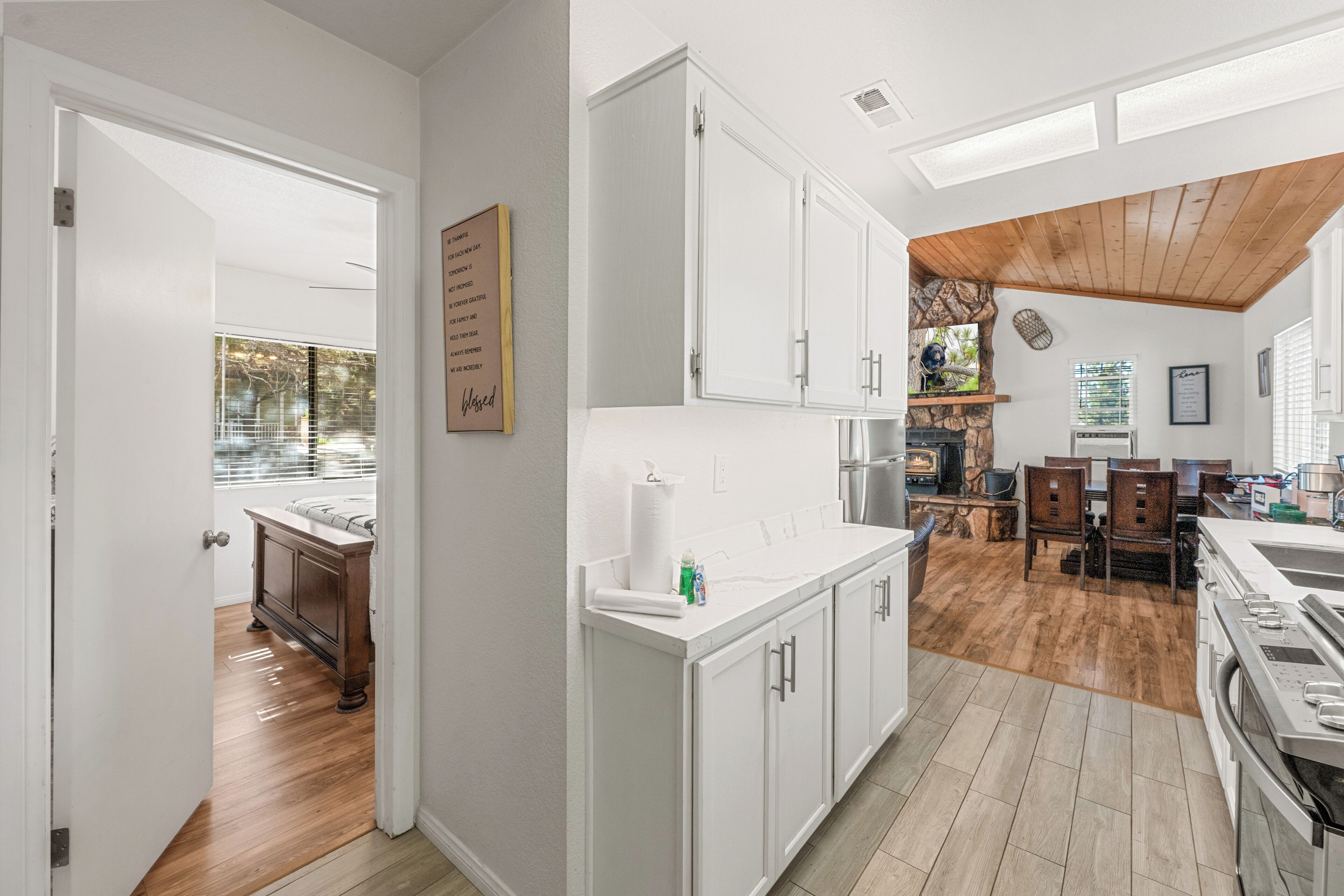 A modern kitchen with white cabinets, a wooden ceiling, and a dining area with a table and chairs.