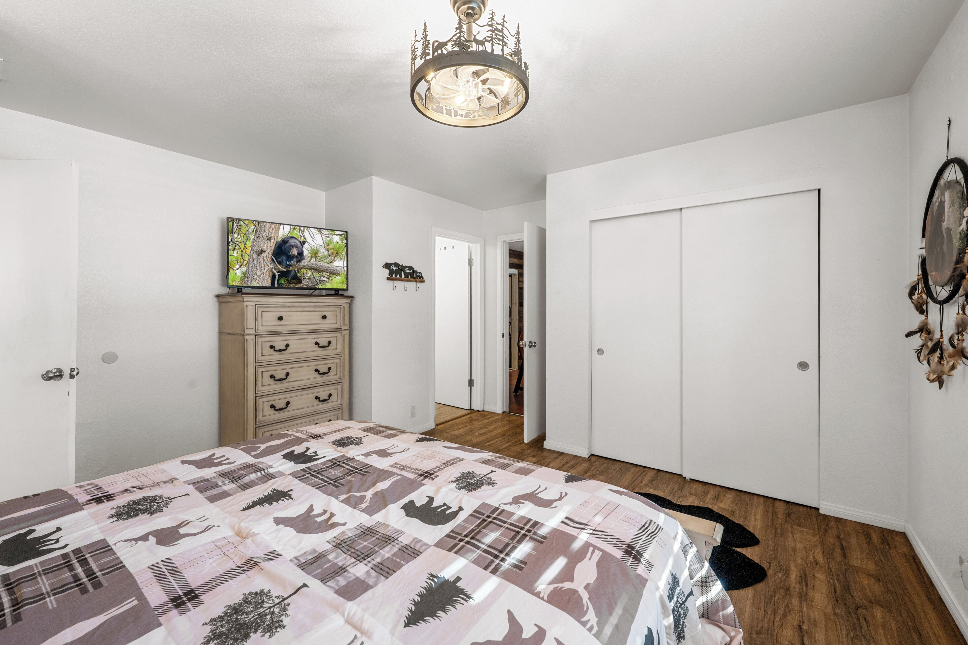 Ein Schlafzimmer mit Bett, Kommode, Fernseher und einer Tür zu einem anderen Raum.