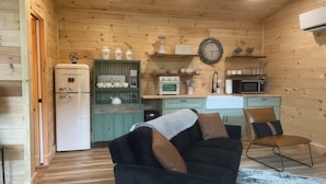 Une chambre confortable, aménagée dans le style d’un chalet, avec un intérieur en bois, une kitchenette, un canapé noir avec des coussins et un tapis à motifs.