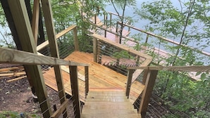 Un escalier en bois mène à une plateforme d’où l’on peut admirer un plan d’eau et la végétation environnante.