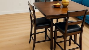 A dining area with a wooden table and four chairs, a vase on the table, and a blue couch in the background.