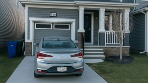 A two-story house with a garage, a driveway, and a silver car parked in front.