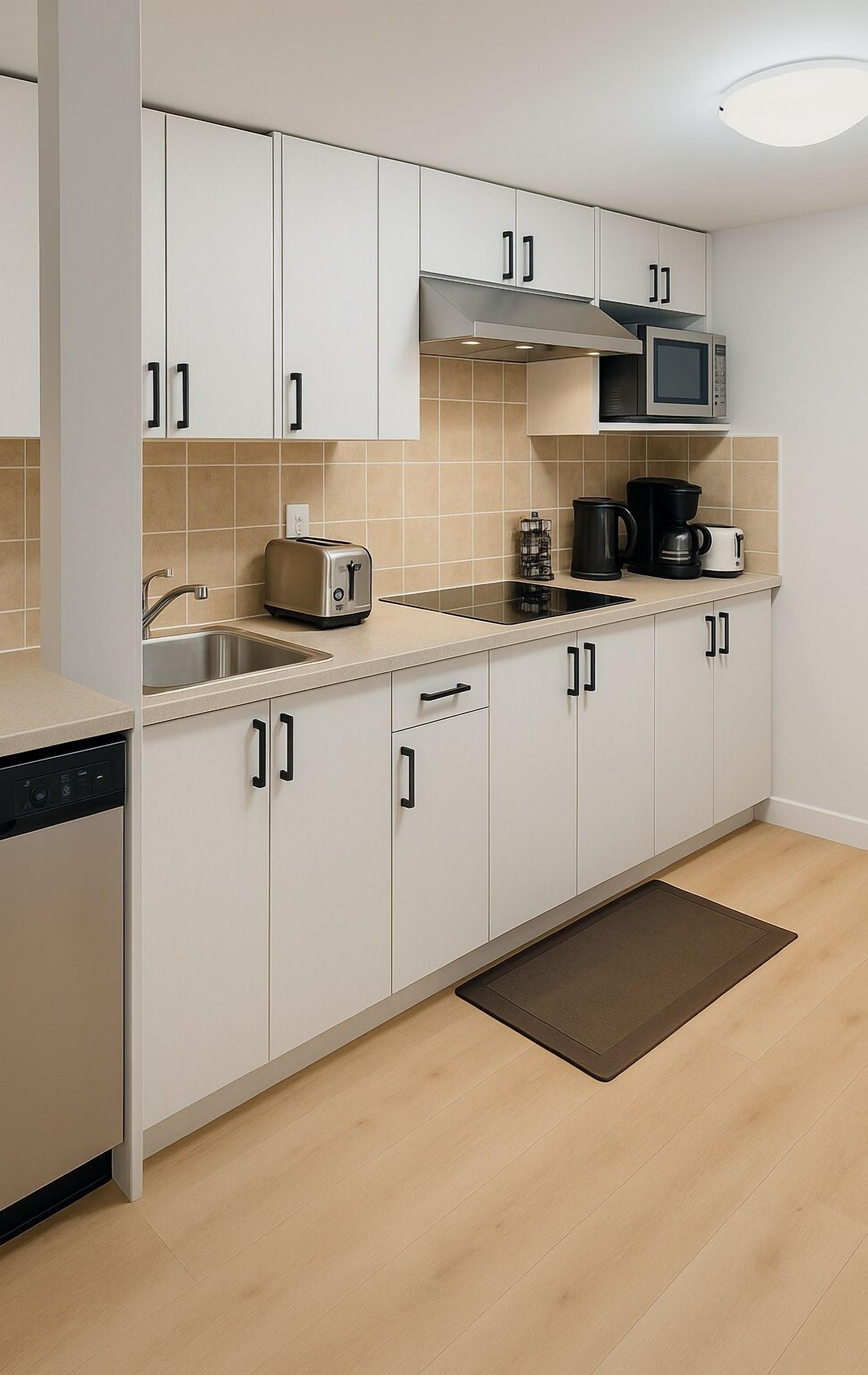 A modern kitchen with white cabinets, a stainless steel sink, a microwave, a toaster, and a coffee maker.