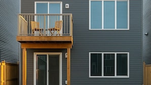 A modern two-story building with a balcony, large windows, and a wooden deck.