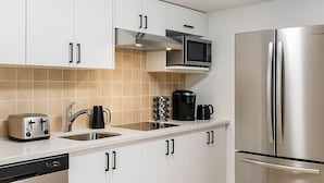 A modern kitchen with white cabinets, a stainless steel refrigerator, a microwave, a toaster, a coffee maker, and a dishwasher.