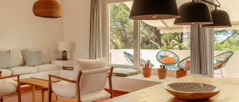 A modern living room with a sofa, chairs, a wooden table, and a large window with curtains.