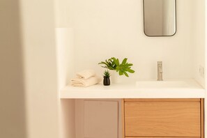 Een badkamer met een wit aanrecht, een wastafel, een spiegel, een plant in pot en netjes opgevouwen handdoeken.