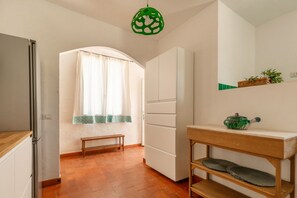 Una cocina con armarios blancos, un banco de madera, una lámpara colgante verde y un pequeño estante con una tetera.