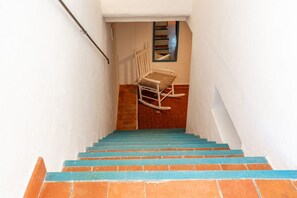 Een trap met blauwe treden die uitkomt op een plateau, waar een witte schommelstoel staat.
