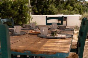 A wooden table with white ceramic cups, a bowl, and a plate with food, set outdoors with chairs and greenery in the background. - CASA BIANCA - Charme and relax between Villasimius and Notteri (Notteri)