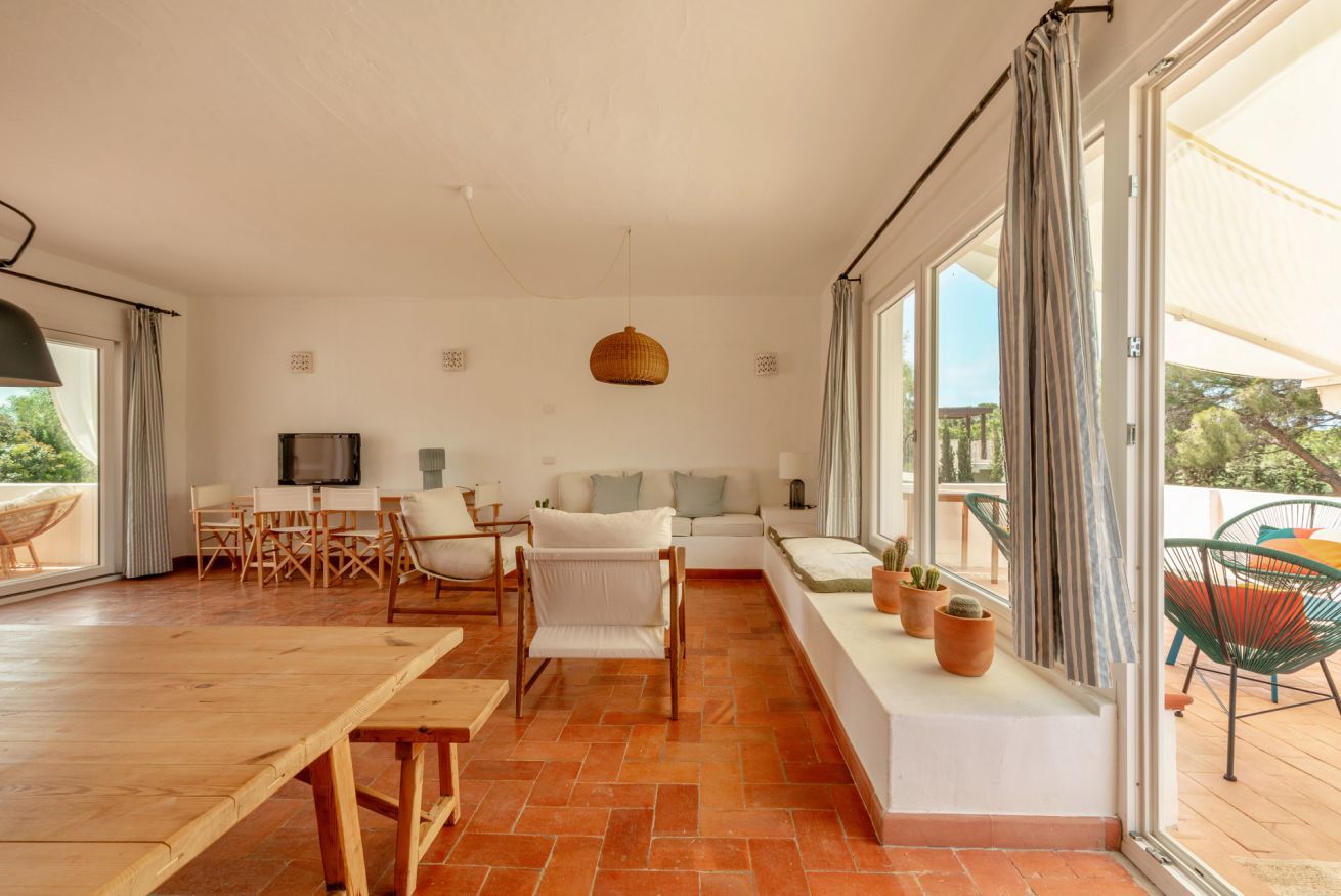 A spacious living area with a wooden dining table, white sofa, and a TV.