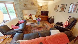 A living room with leather sofas, a coffee table, a stone wall, a television, and framed artwork. - Family home - all comforts, in the heart of Roscoff (Roscoff)