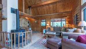 Ein Holzblockhaus-Interieur mit Kamin, Holzmöbeln und Blick ins Freie.