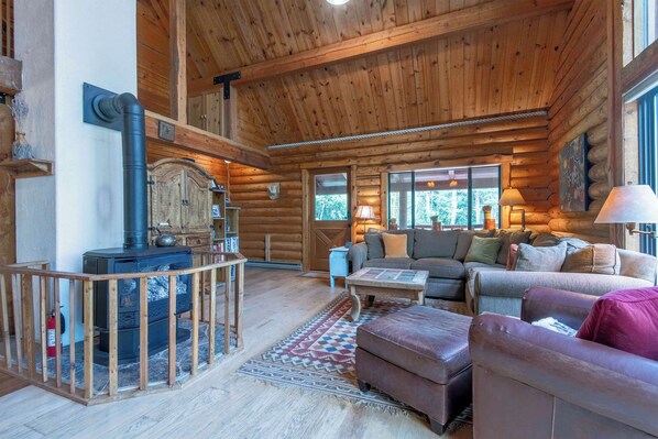 A log cabin interior with a fireplace, wooden furniture, and a view of the outdoors.