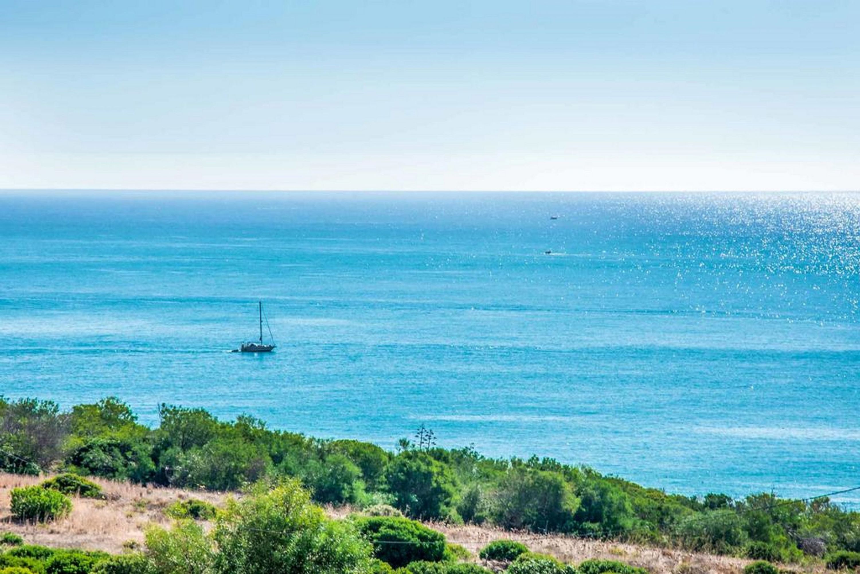 Un paysage côtier offrant une vue dégagée sur la mer et un voilier à l’horizon.