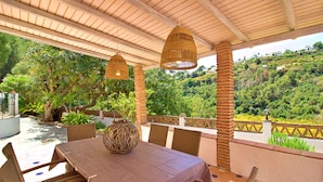 Eine Terrasse im Freien mit Tisch und Stühlen, umgeben von üppiger Vegetation und Blick auf einen Hügel.