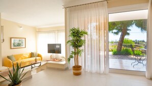 A bright living room with a yellow sofa, a flat-screen TV, and a large window with a view of greenery and a tree. - Villa Marifei in Kato Korakiana (Corfu)