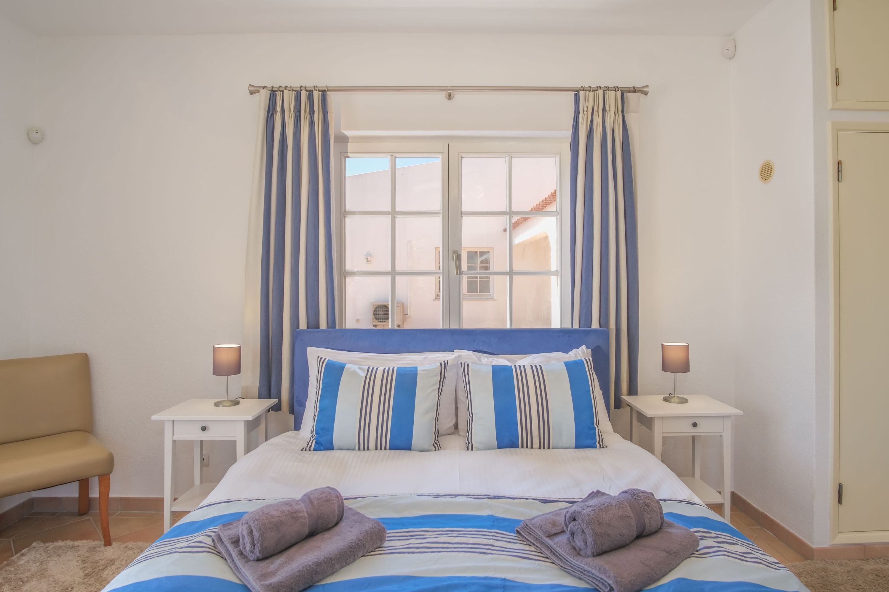 A bedroom with a bed, two bedside tables, a chair, and a window with curtains.