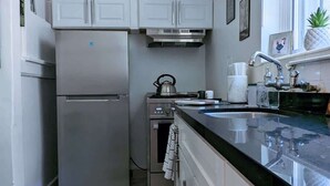 Une cuisine moderne avec des meubles blancs, des appareils en acier inoxydable, un plan de travail noir et une fenêtre équipée de stores.