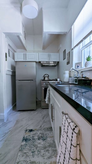 Una cocina moderna con armarios blancos, electrodomésticos de acero inoxidable, encimera negra y ventana con persianas.