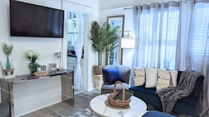 Una sala de estar con sofá, mesa de centro, televisor y planta.
