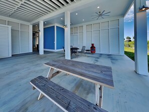 An outdoor patio with a wooden table and benches, surrounded by white walls and blue panels, featuring ceiling fans and recessed lighting. - Casa Abide by Ryson Vacation Rentals (Galveston)