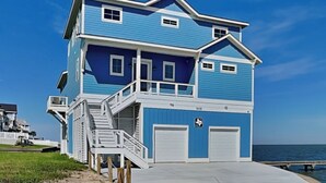 A two-story beach house with a balcony, a staircase, and a garage. - Casa Abide by Ryson Vacation Rentals (Galveston)