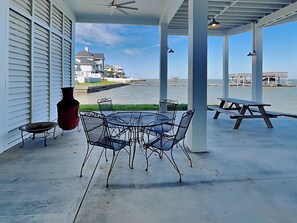 A covered patio with a round table and chairs, a red vase, and a small table with a chair. - Casa Abide by Ryson Vacation Rentals (Galveston)