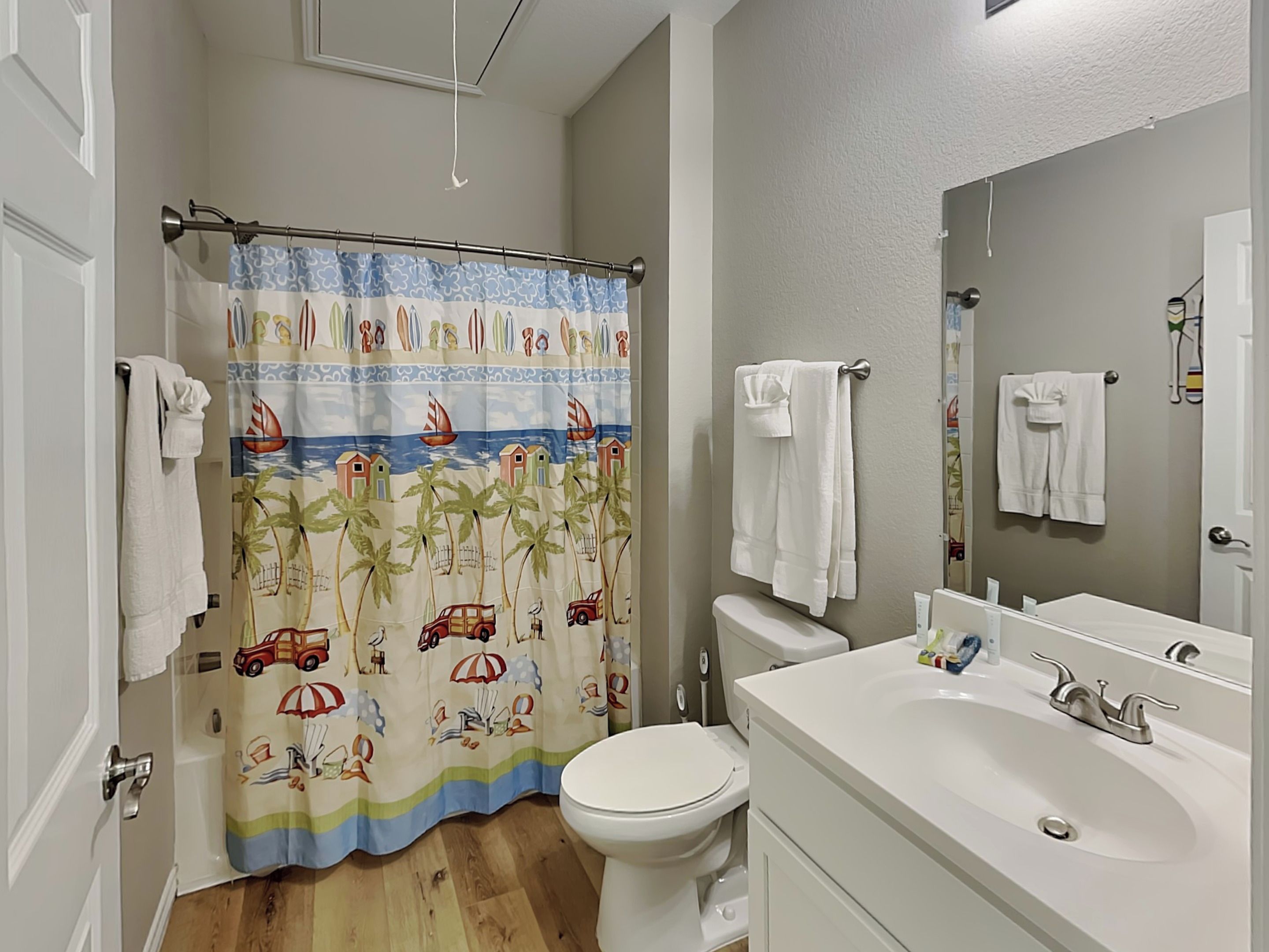 Un baño con cortina de ducha con diseño tropical, inodoro, lavabo con espejo y toallas colgadas en la pared.