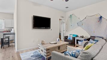 A living room with a TV mounted on the wall, a wooden coffee table, a grey sofa, and a netted wall decoration.