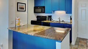 A kitchen with blue cabinets, a granite countertop, a microwave, a coffee maker, and a dishwasher. - Seventh Heaven by Ryson Vacation Rentals (Galveston)