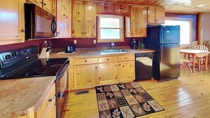 Une cuisine avec des meubles de rangement en bois, un réfrigérateur noir, une cuisinière et un évier.